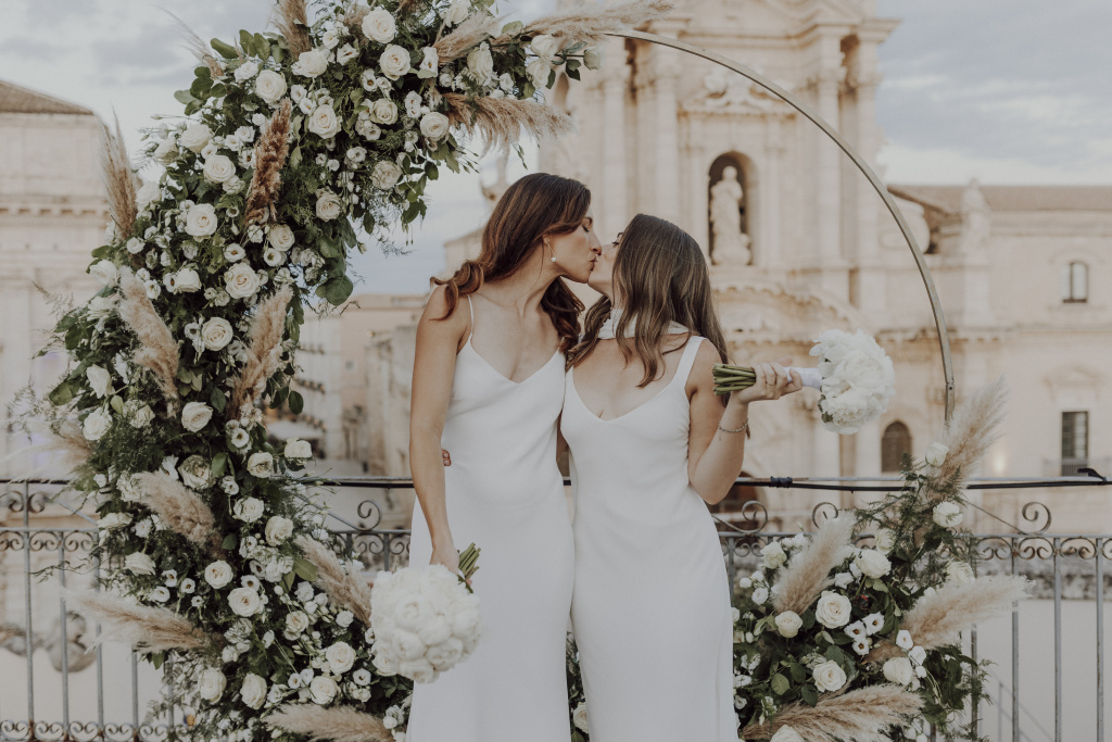 Two brides standing before officiant in Ortigia island Syracuse, lgbtq+ luxury wedding Sicily
